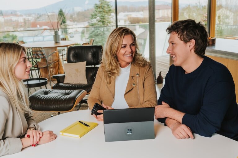 Eine Frau berät 2 Menschen an einem Tisch mit Laptop und Notizbuch