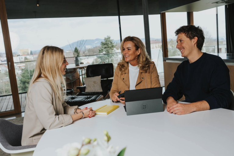 3 Menschen sitzen an einem Tisch mit einem Laptop und besprechen sich.